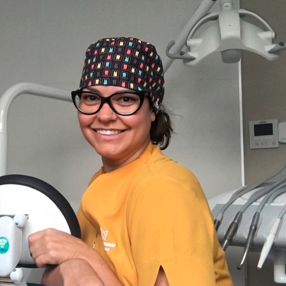 La Dra. Beatriz Tomás, con uniforme amarillo, gorro quirúrgico y gafas, sonriendo en uno de los gabinetes de la clínica