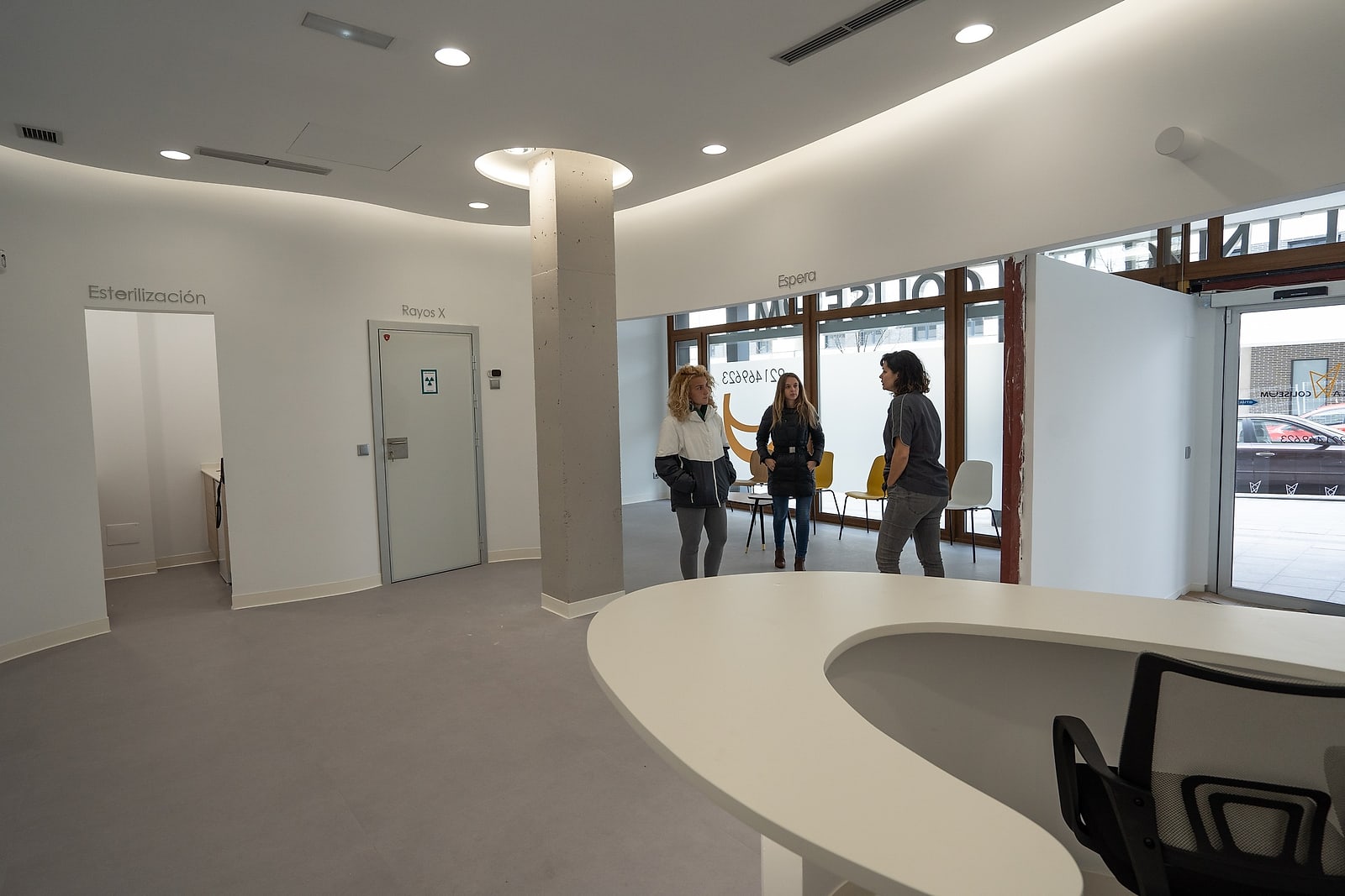 Sala de espera de Clínica Coliseum, con sillas amarillas junto al ventanal que da a la calle y acceso a ras de suelo